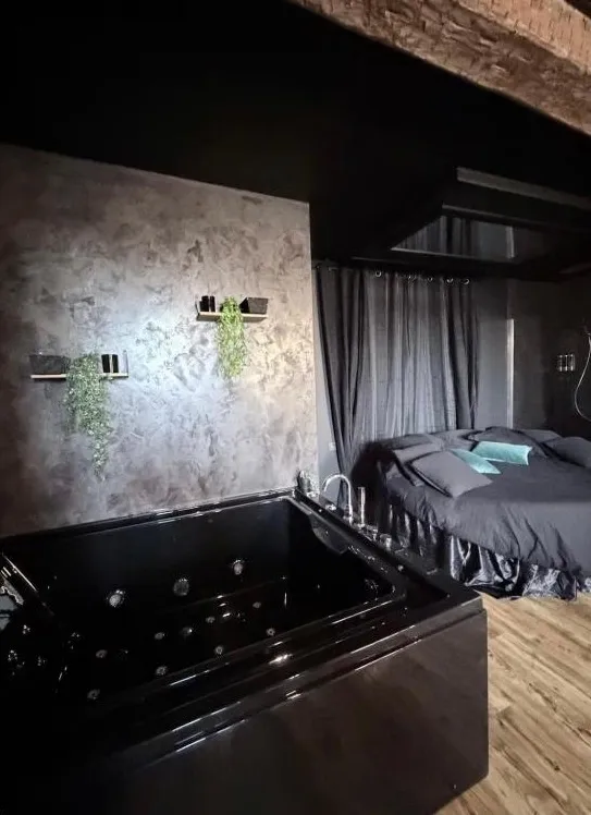 La baignoire balnéo noire au premier plan et le lit rond au fond