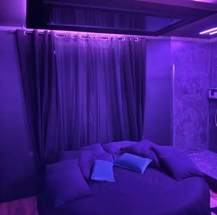 Le lit rond de la love room sous un éclairage violet, miroir au plafond